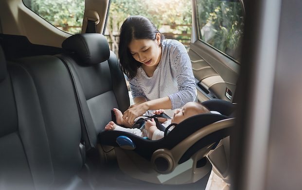 Young Asian woman strapping a Asian baby into a carseat.
